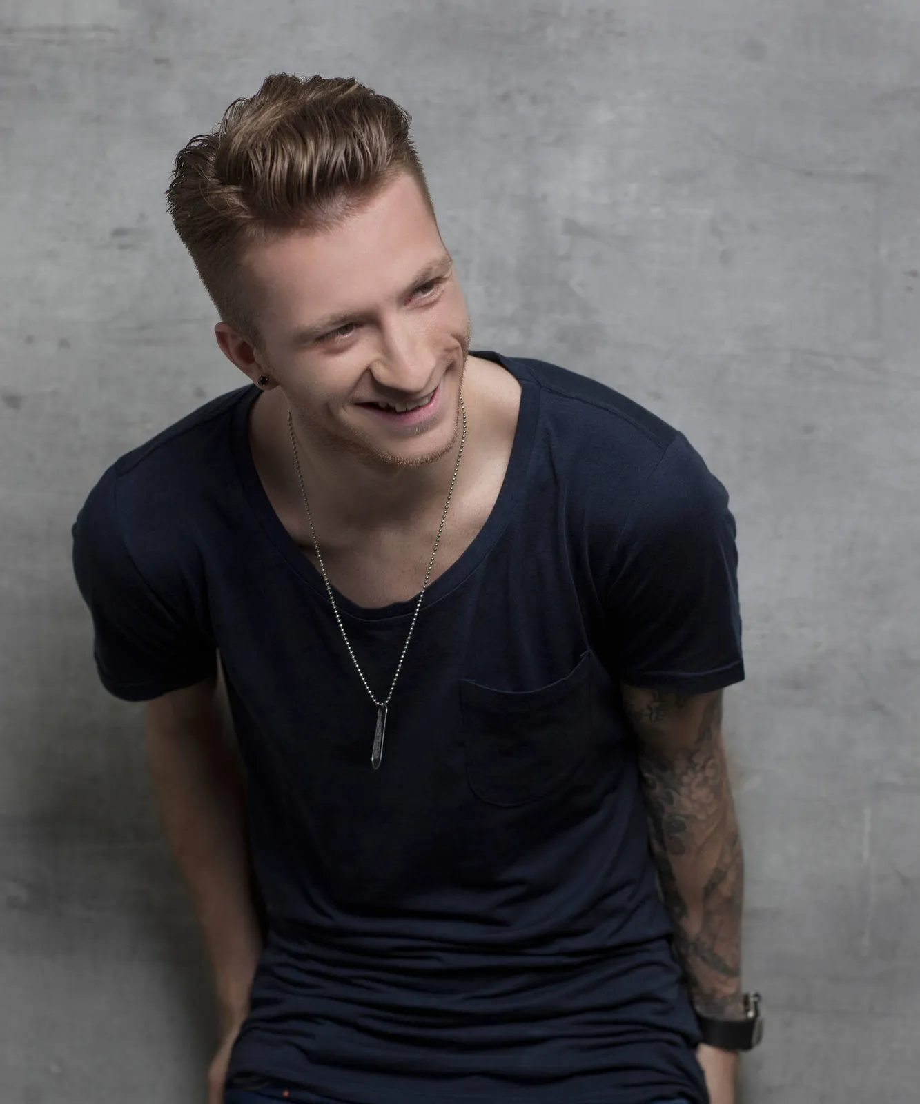 Marco Reus sitzt vor einer Betonwand und lacht zur Seite